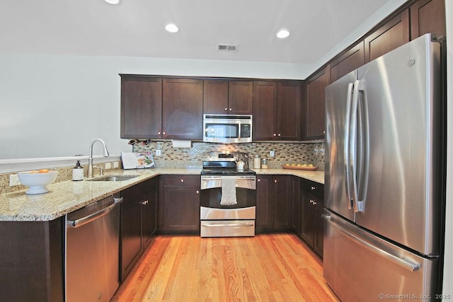 kitchen with appliances with stainless steel finishes, sink, decorative backsplash, light stone counters, and light wood-type flooring