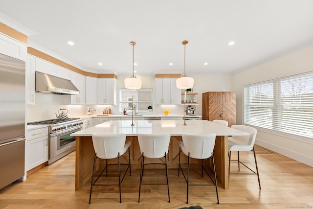 kitchen featuring premium appliances, pendant lighting, light countertops, an island with sink, and extractor fan