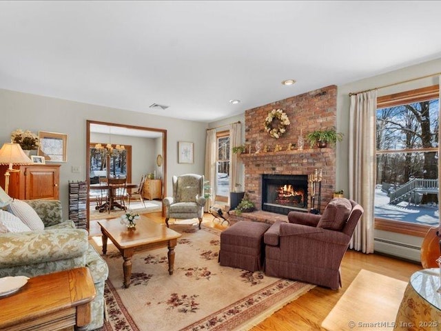 living room with light wood finished floors, visible vents, a baseboard radiator, a fireplace, and a chandelier