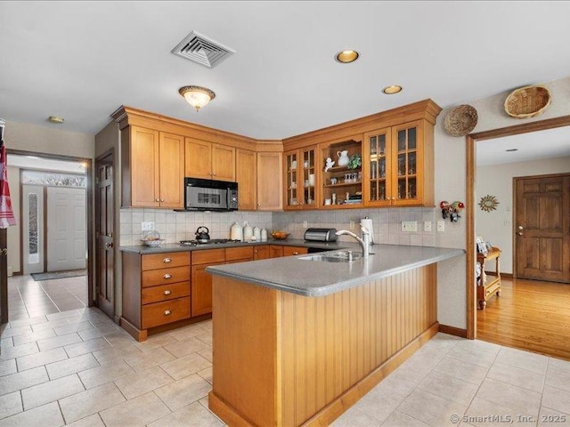 kitchen featuring a peninsula, a sink, visible vents, backsplash, and brown cabinets