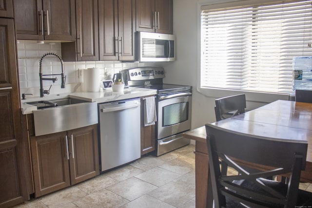 kitchen featuring dark brown cabinetry, a sink, light countertops, appliances with stainless steel finishes, and decorative backsplash