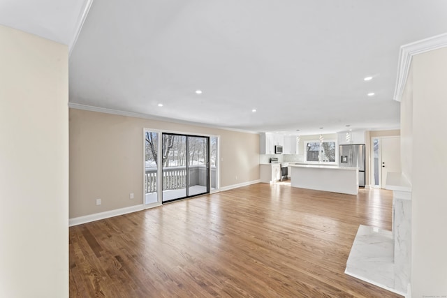 unfurnished living room with baseboards, crown molding, and light wood finished floors