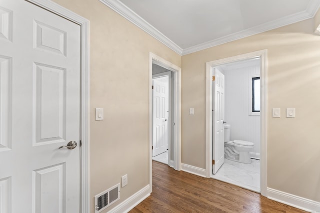 hallway featuring baseboards, crown molding, wood finished floors, and visible vents