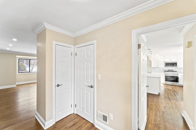 hallway with visible vents, baseboards, wood finished floors, and crown molding