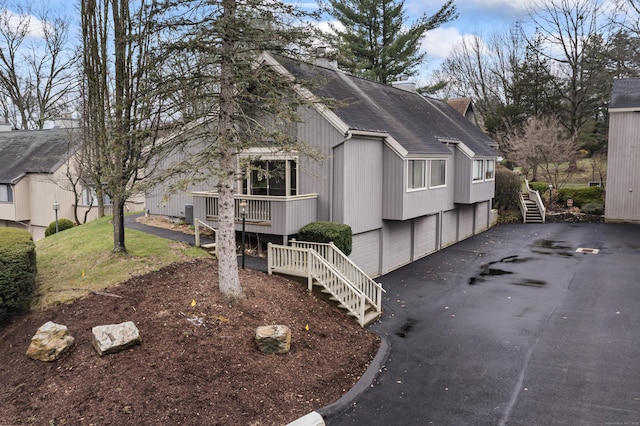 view of property exterior with stairway, driveway, roof with shingles, and a chimney