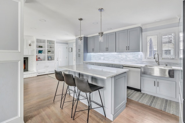 kitchen featuring a kitchen island, decorative light fixtures, stainless steel dishwasher, light stone counters, and a brick fireplace