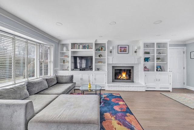 living room featuring hardwood / wood-style flooring, crown molding, built in features, and a fireplace