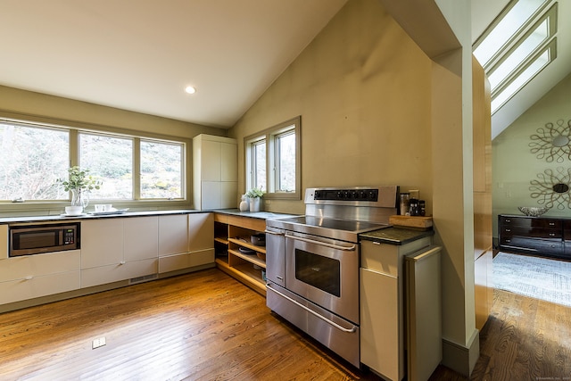kitchen with dark countertops, light wood finished floors, lofted ceiling, stainless steel appliances, and recessed lighting