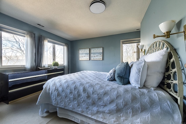 carpeted bedroom featuring multiple windows, a textured ceiling, and visible vents