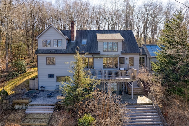 rear view of house featuring a shingled roof, a wooden deck, stairway, and a chimney