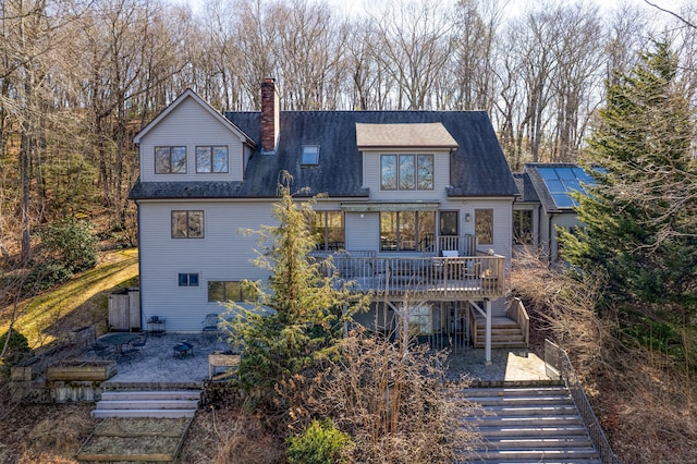 rear view of house with a shingled roof, a wooden deck, stairs, and a chimney