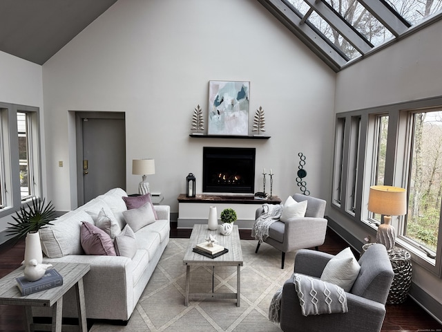 living area featuring high vaulted ceiling, a lit fireplace, a skylight, and wood finished floors