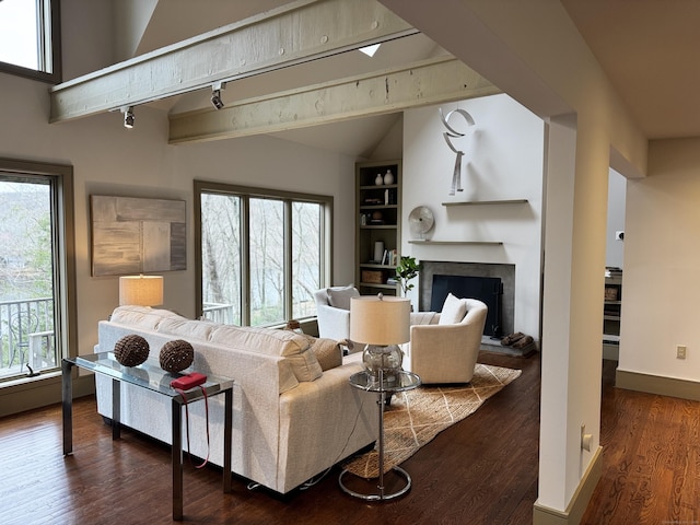 living room with lofted ceiling with beams, a fireplace with raised hearth, built in shelves, baseboards, and wood finished floors