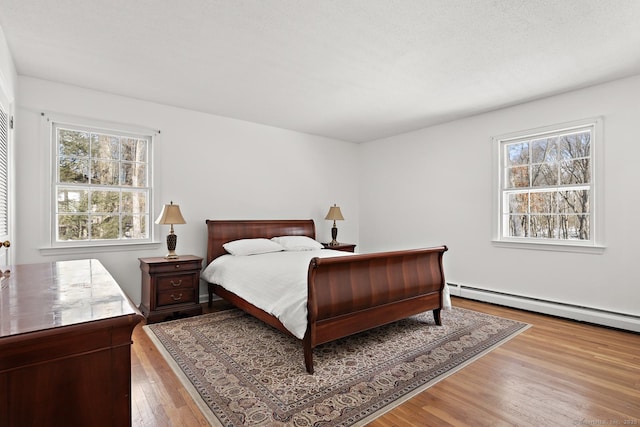 bedroom with multiple windows, a baseboard heating unit, and hardwood / wood-style flooring