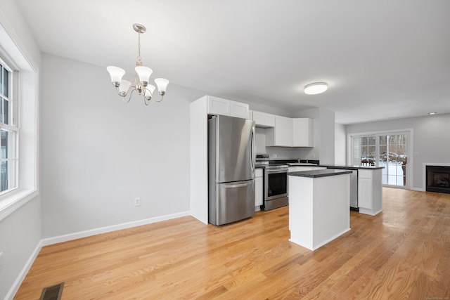 kitchen with white cabinetry, stainless steel appliances, light hardwood / wood-style floors, and hanging light fixtures