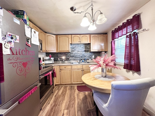 kitchen with appliances with stainless steel finishes, decorative light fixtures, light brown cabinetry, and light hardwood / wood-style floors