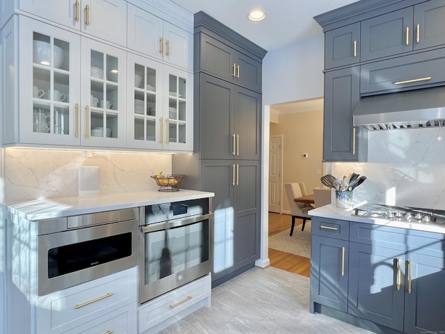 kitchen with decorative backsplash, ornamental molding, wall chimney exhaust hood, stainless steel appliances, and light hardwood / wood-style flooring