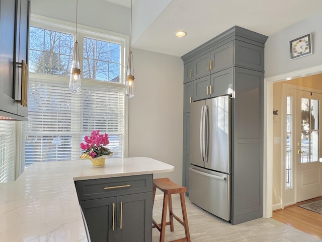 kitchen with a kitchen breakfast bar, gray cabinetry, light stone counters, and stainless steel refrigerator