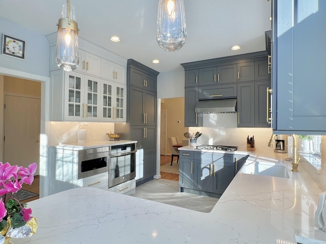 kitchen featuring wall chimney exhaust hood, stainless steel gas cooktop, pendant lighting, decorative backsplash, and white cabinets