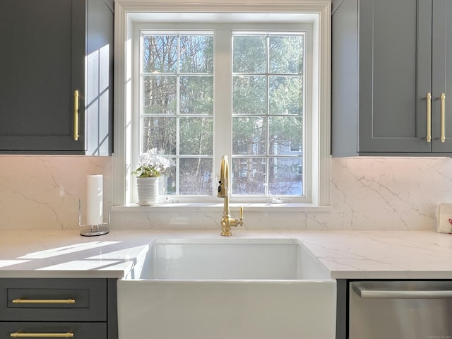 interior details with tasteful backsplash, light stone countertops, gray cabinets, and stainless steel dishwasher