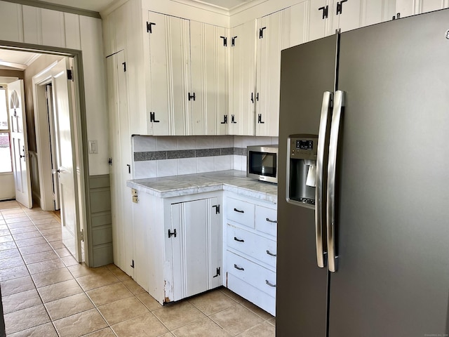 kitchen with light tile patterned flooring, crown molding, white cabinets, stainless steel appliances, and backsplash