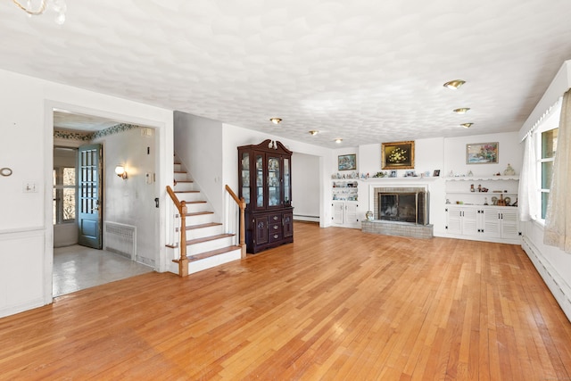 unfurnished living room with light wood-type flooring, baseboard heating, stairway, and a fireplace