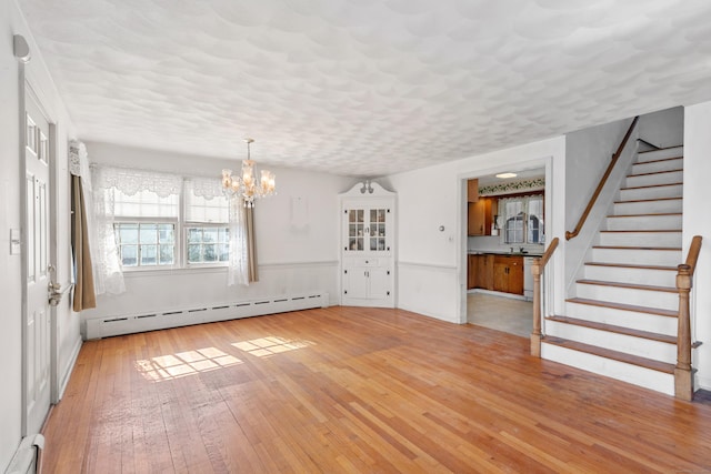 empty room featuring a baseboard radiator, stairway, an inviting chandelier, light wood-style floors, and a baseboard heating unit