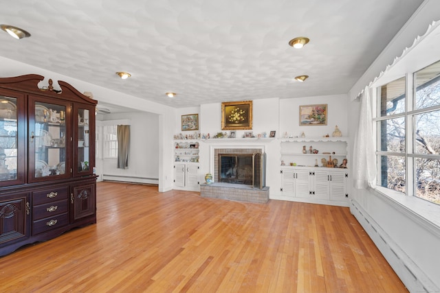 unfurnished living room featuring light wood finished floors, baseboard heating, and a wealth of natural light