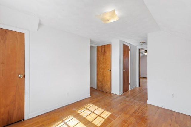 empty room featuring a baseboard radiator, baseboards, vaulted ceiling, and hardwood / wood-style floors