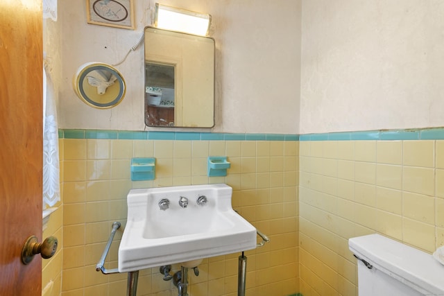 half bathroom featuring toilet, wainscoting, a sink, and tile walls