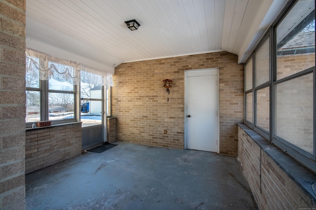 empty room with vaulted ceiling, brick wall, and unfinished concrete floors