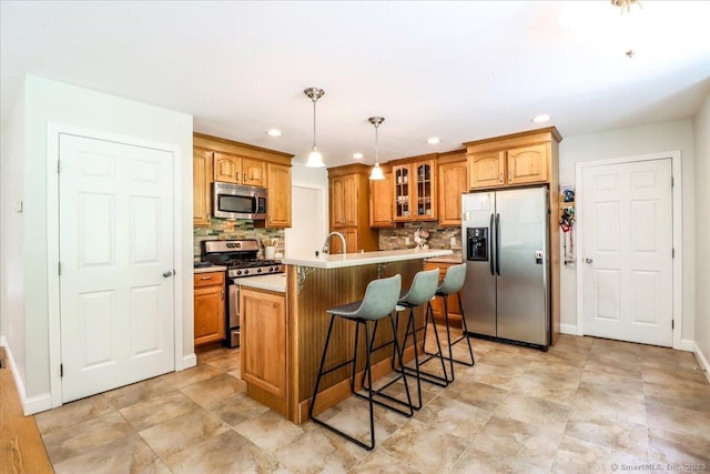 kitchen featuring appliances with stainless steel finishes, backsplash, a kitchen breakfast bar, an island with sink, and decorative light fixtures