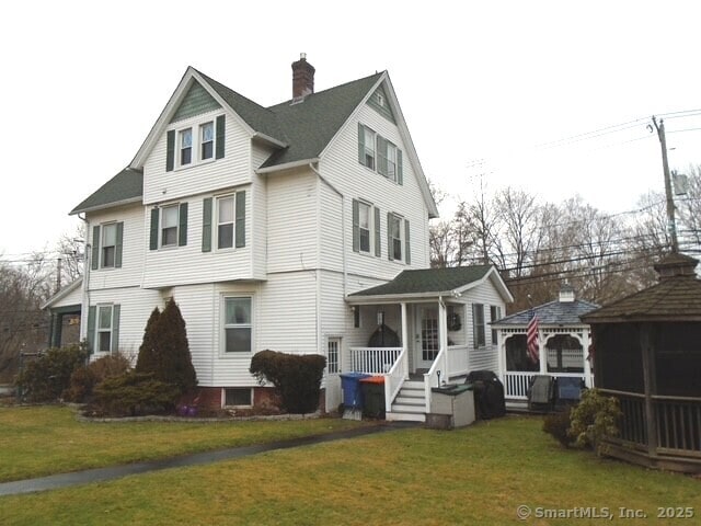 view of front of property featuring covered porch, a gazebo, a front lawn, and a chimney