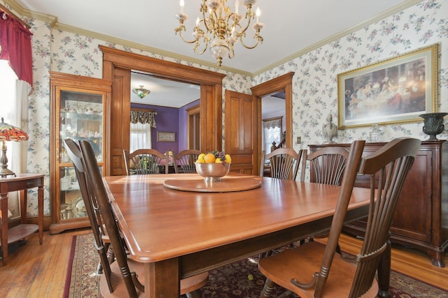 dining room featuring crown molding, a chandelier, wood finished floors, and wallpapered walls