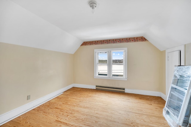 additional living space with baseboard heating, vaulted ceiling, and light hardwood / wood-style flooring