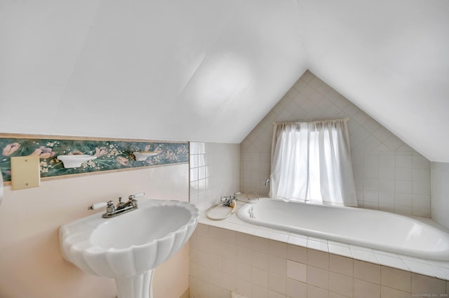 bathroom with sink, vaulted ceiling, and tiled tub