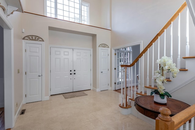 foyer featuring visible vents, a towering ceiling, baseboards, and stairs