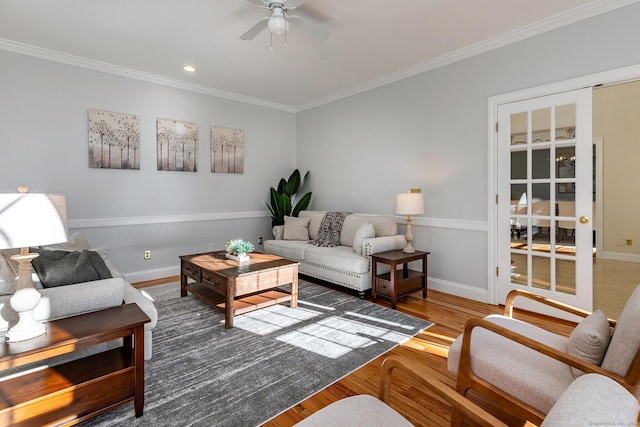 living room featuring a ceiling fan, crown molding, baseboards, and wood finished floors