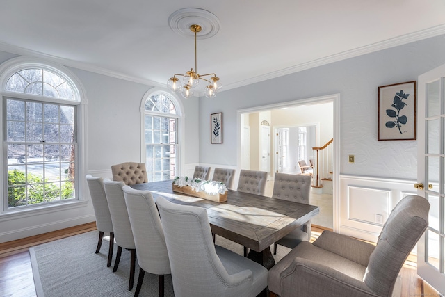 dining space with a wainscoted wall, wood finished floors, ornamental molding, stairway, and an inviting chandelier