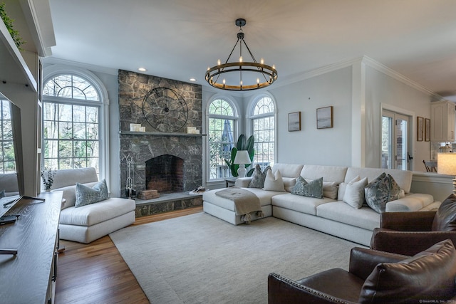 living room with wood finished floors, crown molding, a stone fireplace, a notable chandelier, and recessed lighting