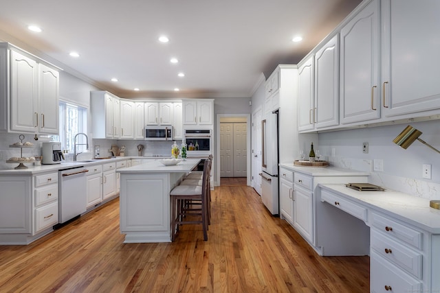 kitchen with white appliances, white cabinets, light wood-type flooring, a kitchen bar, and a sink