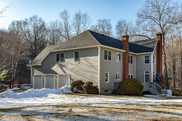 view of snow covered exterior with an attached garage, a chimney, and roof with shingles