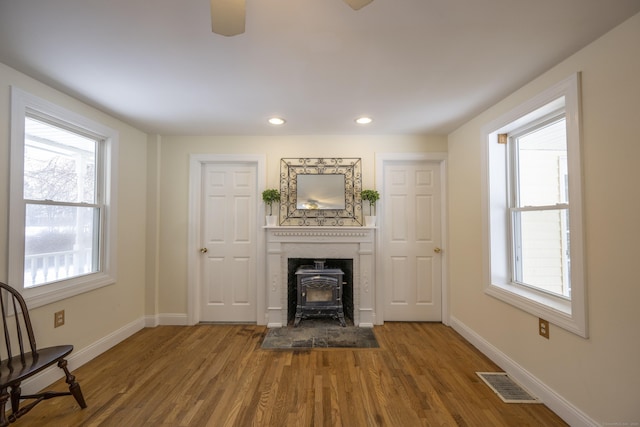 unfurnished living room with wood finished floors, a wood stove, baseboards, and visible vents