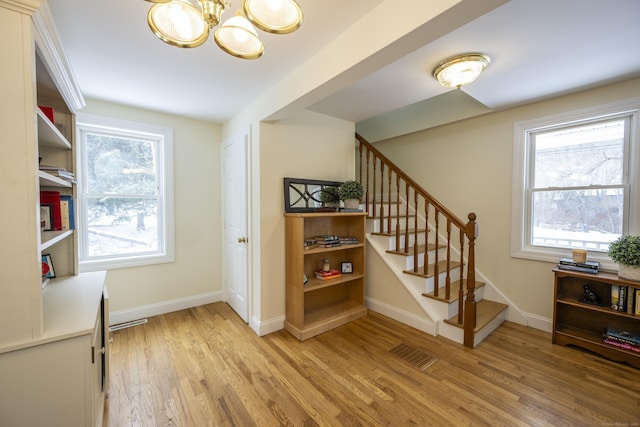 staircase featuring an inviting chandelier, wood finished floors, visible vents, and a healthy amount of sunlight