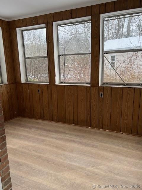 unfurnished room with a wealth of natural light, light hardwood / wood-style floors, and wood walls