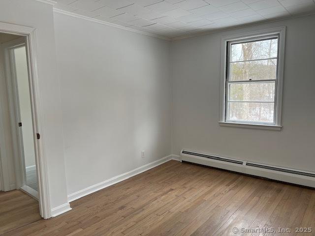 unfurnished room with a baseboard heating unit, crown molding, and light hardwood / wood-style floors