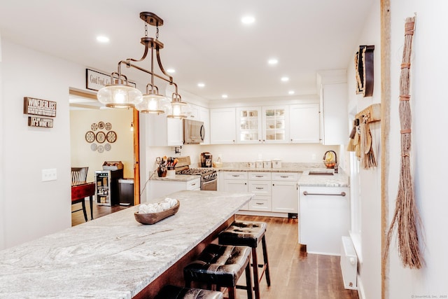 kitchen featuring appliances with stainless steel finishes, pendant lighting, white cabinetry, wood-type flooring, and sink