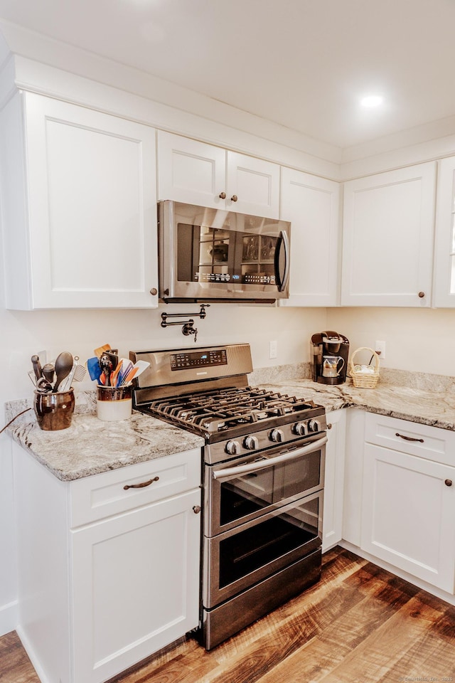 kitchen with stainless steel appliances, light stone countertops, light hardwood / wood-style floors, and white cabinets