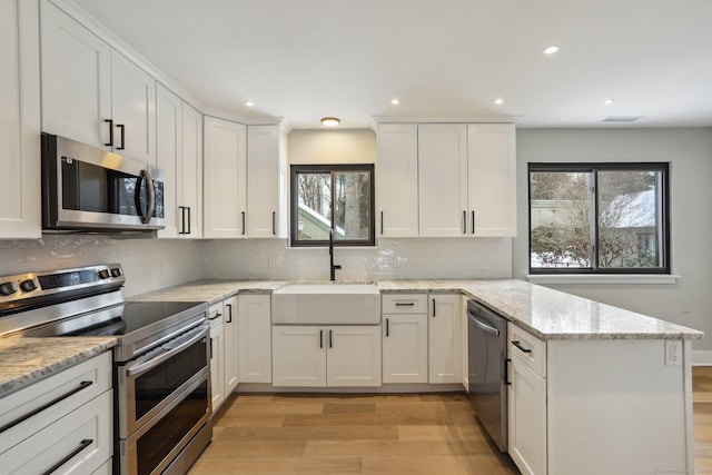 kitchen featuring sink, white cabinetry, stainless steel appliances, light stone countertops, and a healthy amount of sunlight