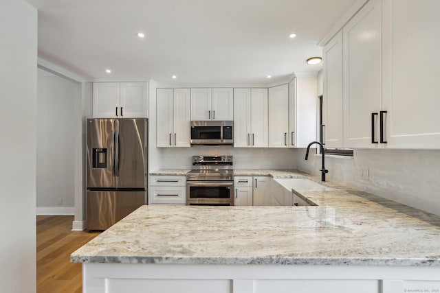 kitchen featuring appliances with stainless steel finishes, light stone countertops, decorative backsplash, and white cabinets